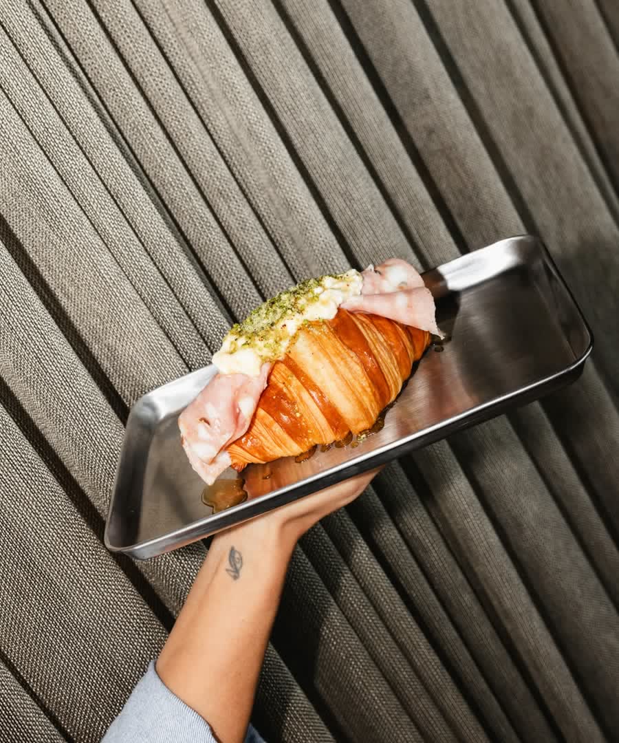A croissant topped with chopped pistachio, held on a steel tray.