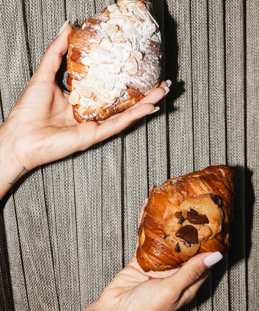 Two hands holding an almond croissant and a cookie.